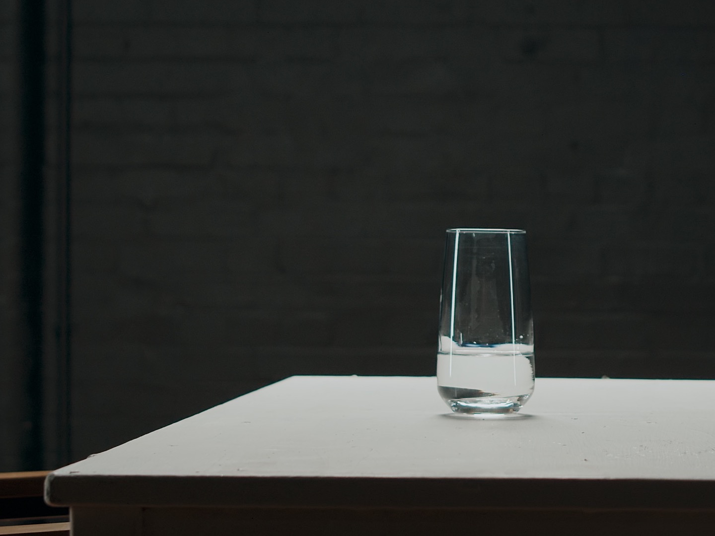 The table and two glasses seen from further back, small against the black room.