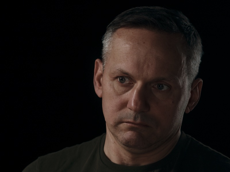 Mirek in close-up, lit against the dark room.
