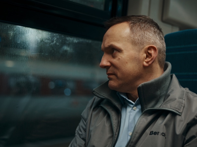 Mirek on a train, looking out of a rain-streaked window.