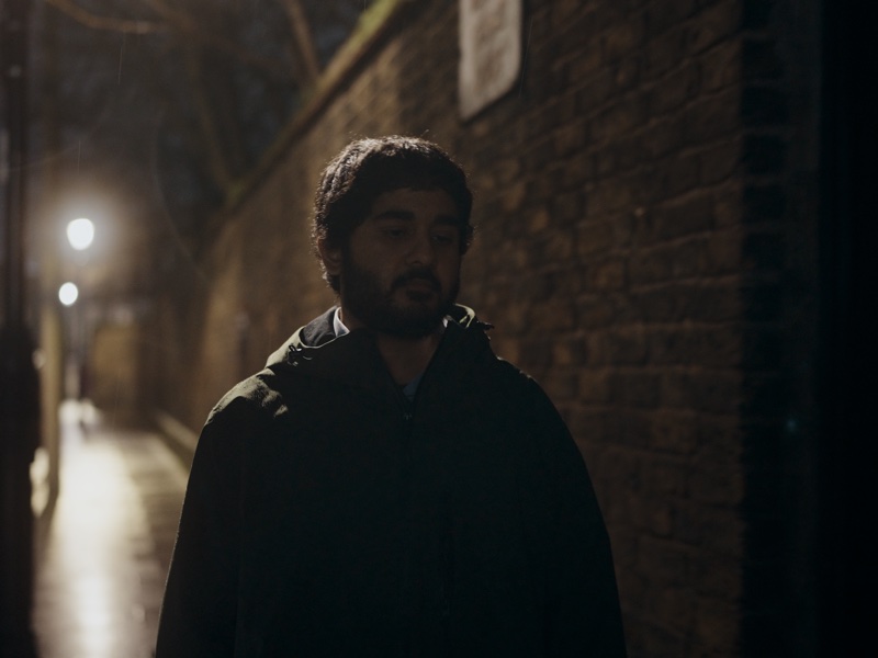 Sohail walking down a narrow brick alley at night.